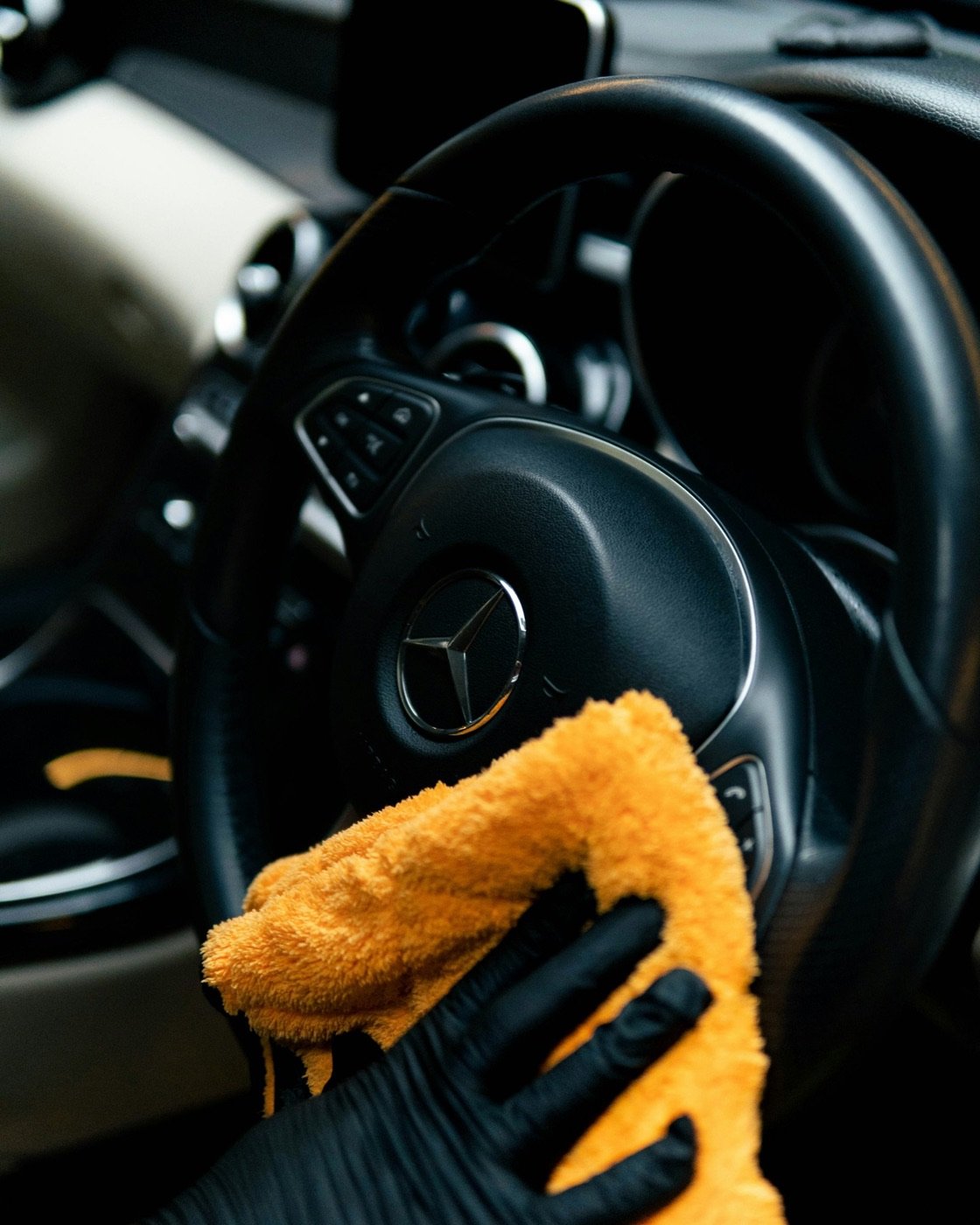 Gloved hand wiping a steering wheel with a microfibre cloth